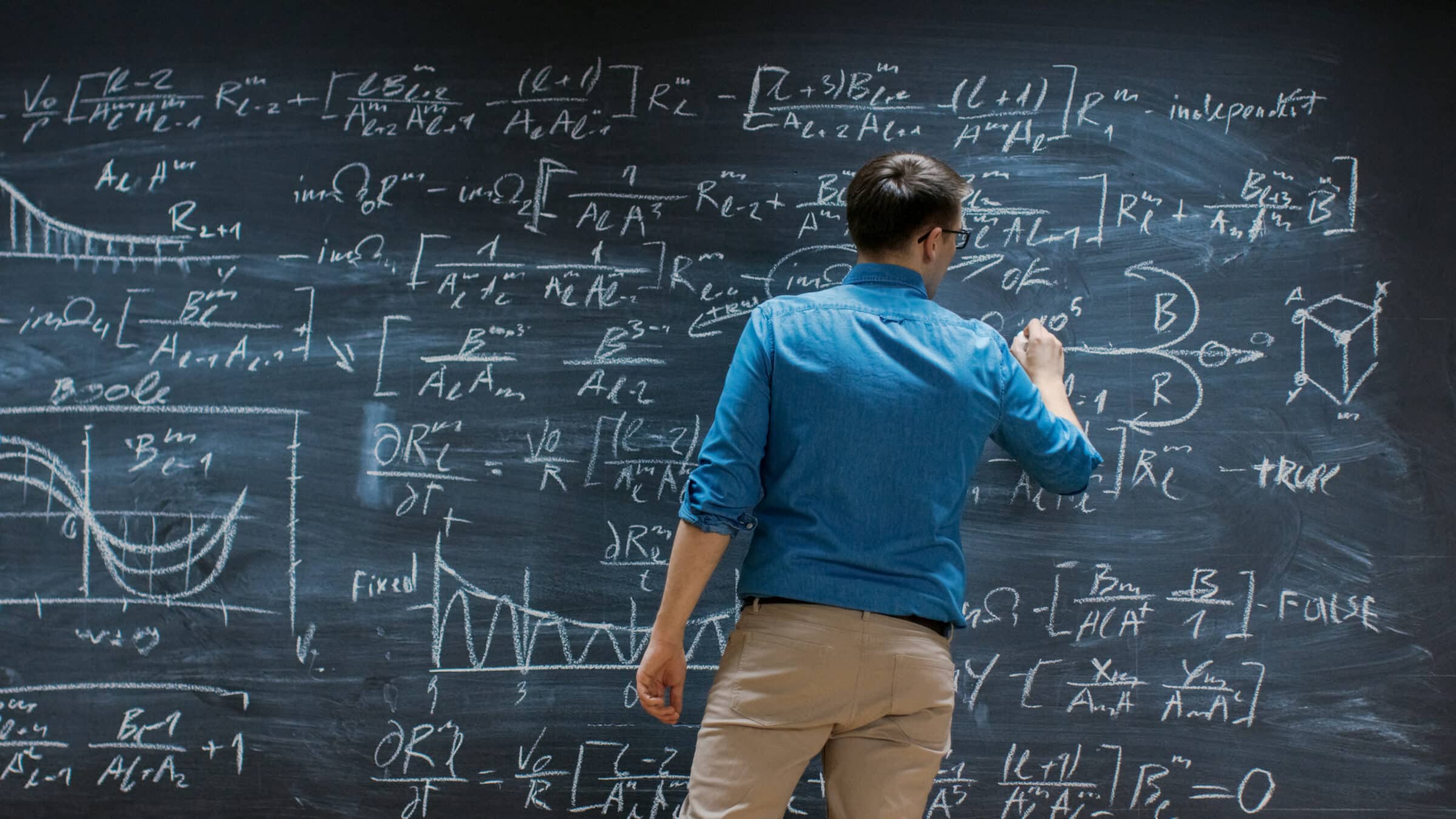Brilliant Young Mathematician Is Writing on Big Blackboard and Thinking about Solving Long and Complex Equation/ Formula.